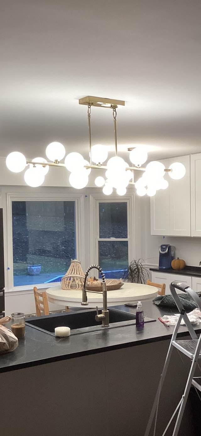 Bright kitchen with island, hanging globe lights, sink, windows, and a folded step ladder near the counter