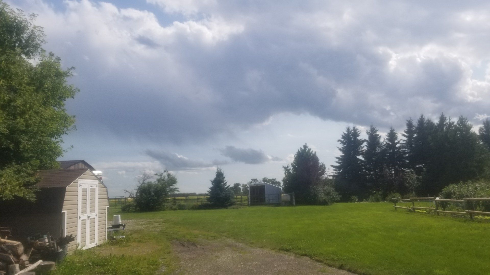 A shed in the middle of a grassy field with a cloudy sky in the background.