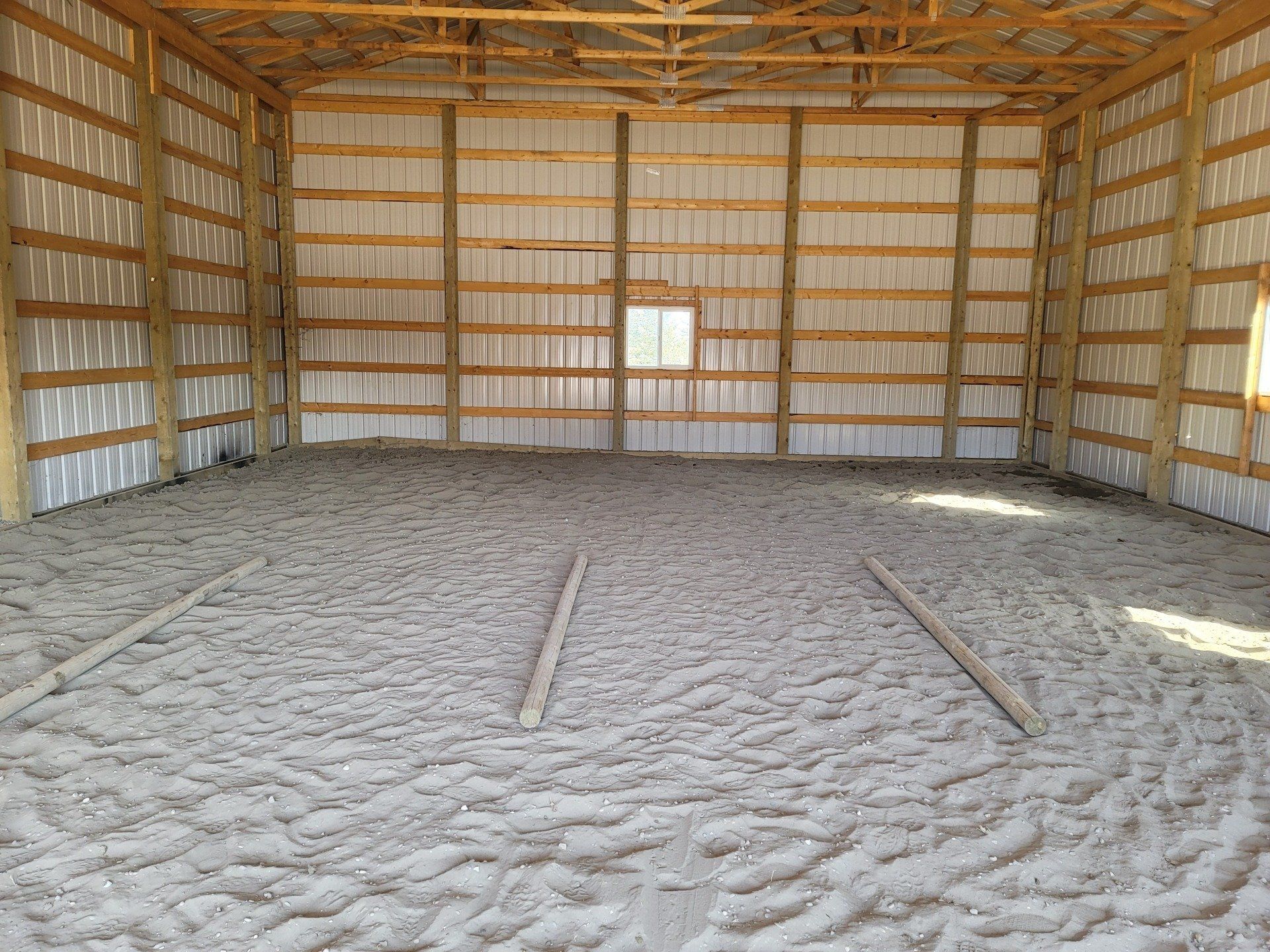 Empty wooden barn interior with hay bale walls and a dirt floor.