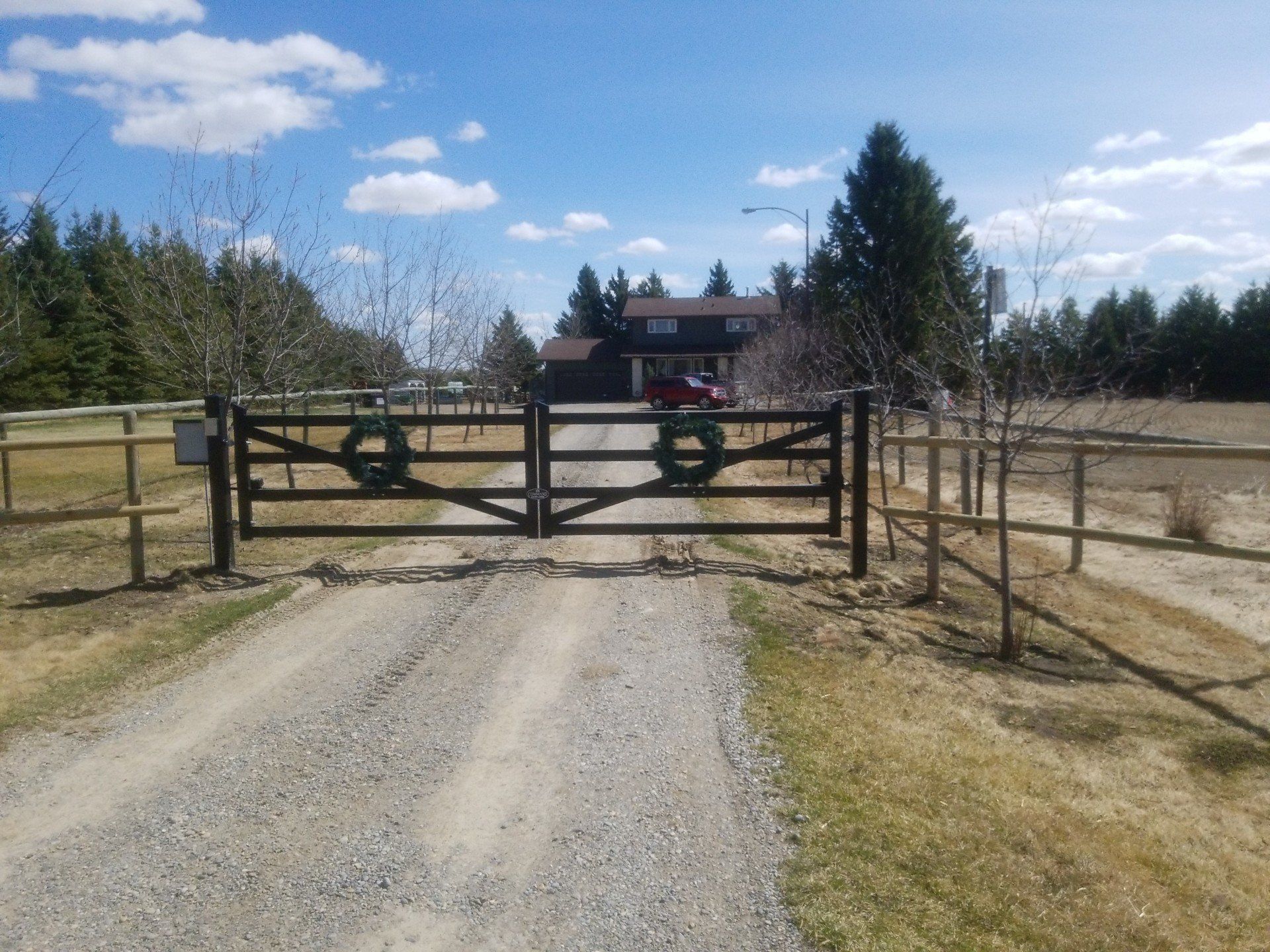 A dirt road with a fence and a gate leading to a house.