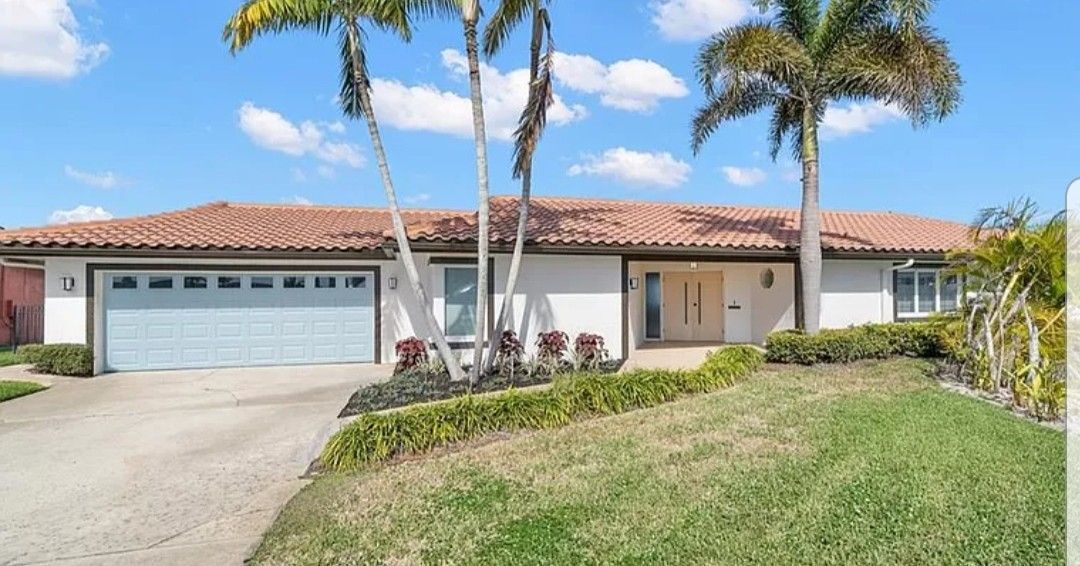 Ranch-style house with a terracotta roof, blue garage door, and palm trees on a sunny day.