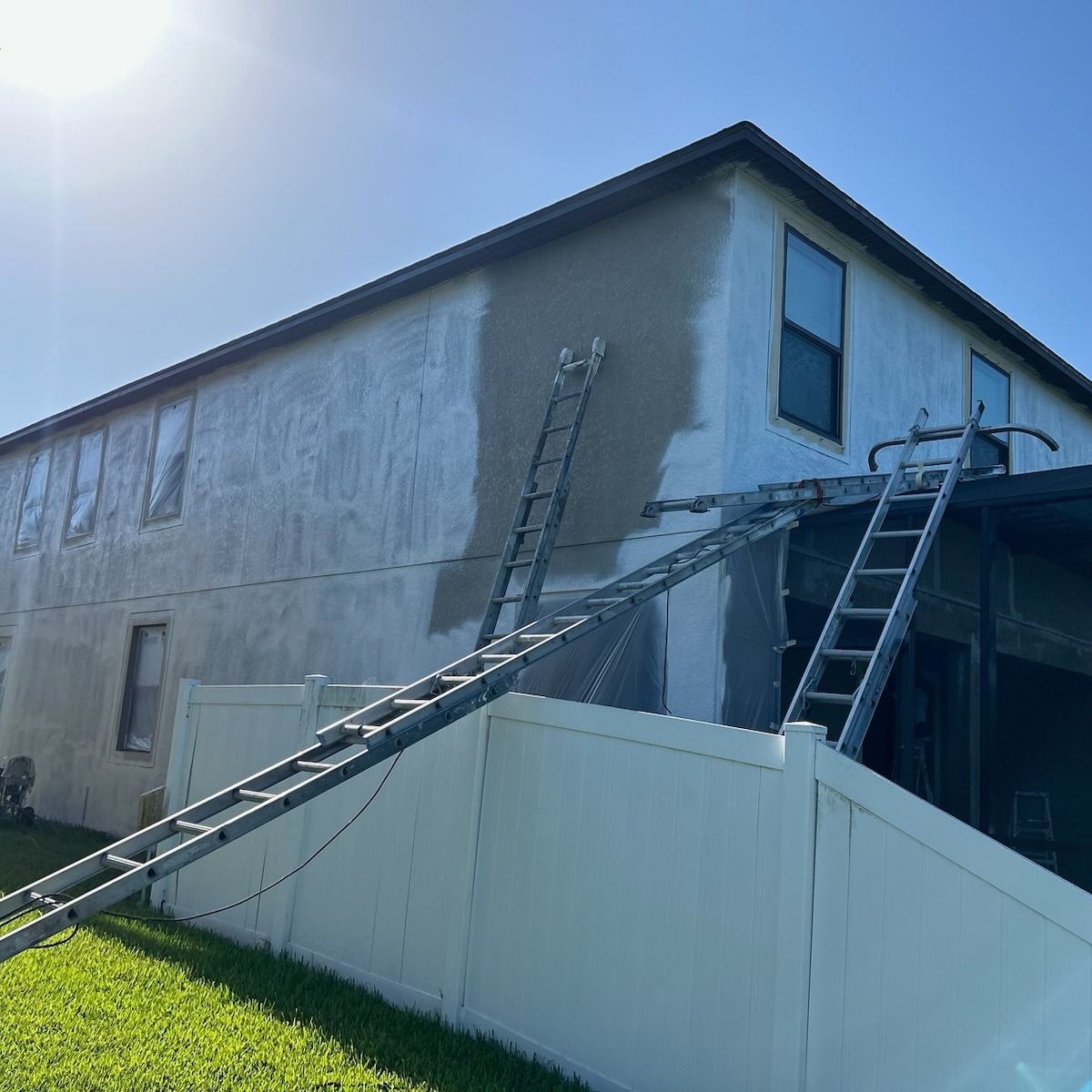 Ladders leaning against a two-story house being repaired, with patches of new stucco on the exterior wall.