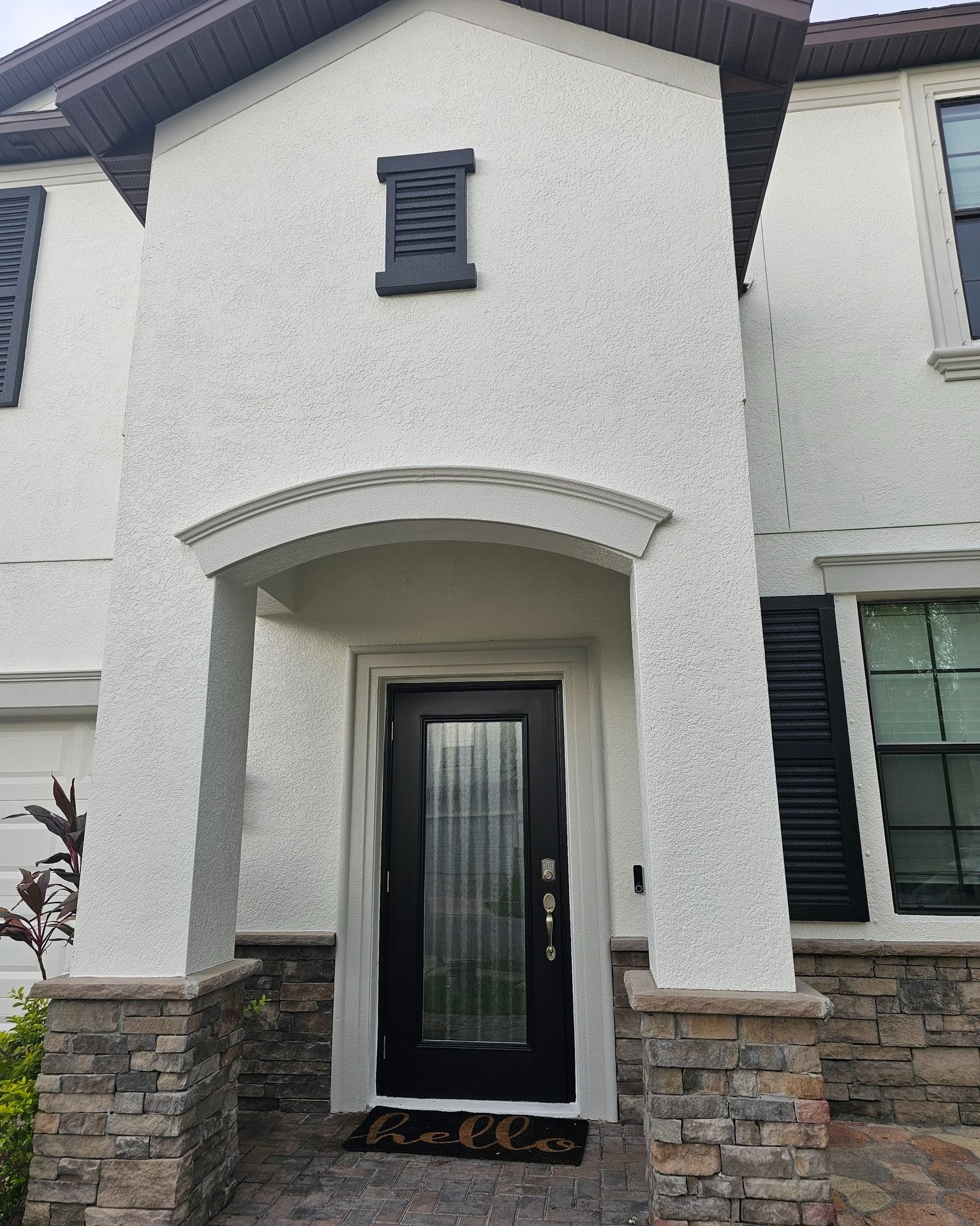 White stucco house with black door, shutters, and stone base. 