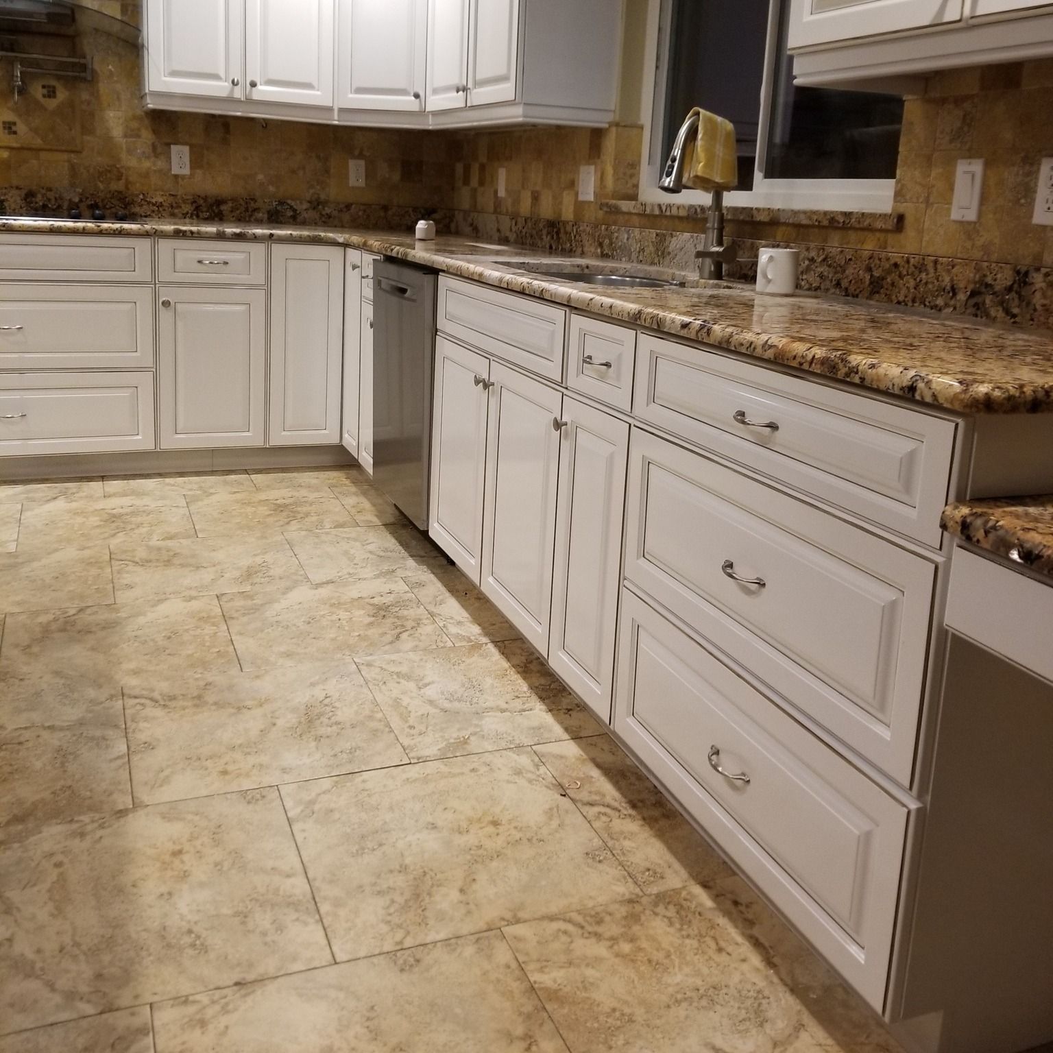 White kitchen cabinets with a granite countertop, stainless steel dishwasher, and tile flooring.