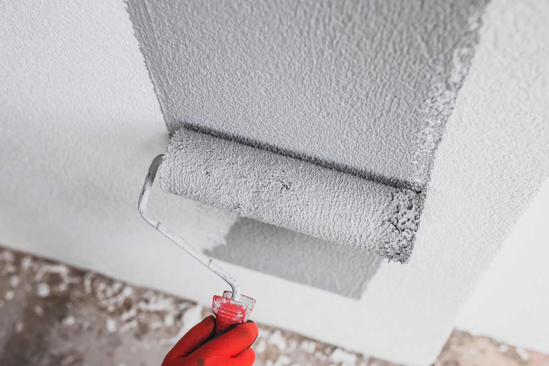 Person in red glove painting ceiling with gray paint roller.