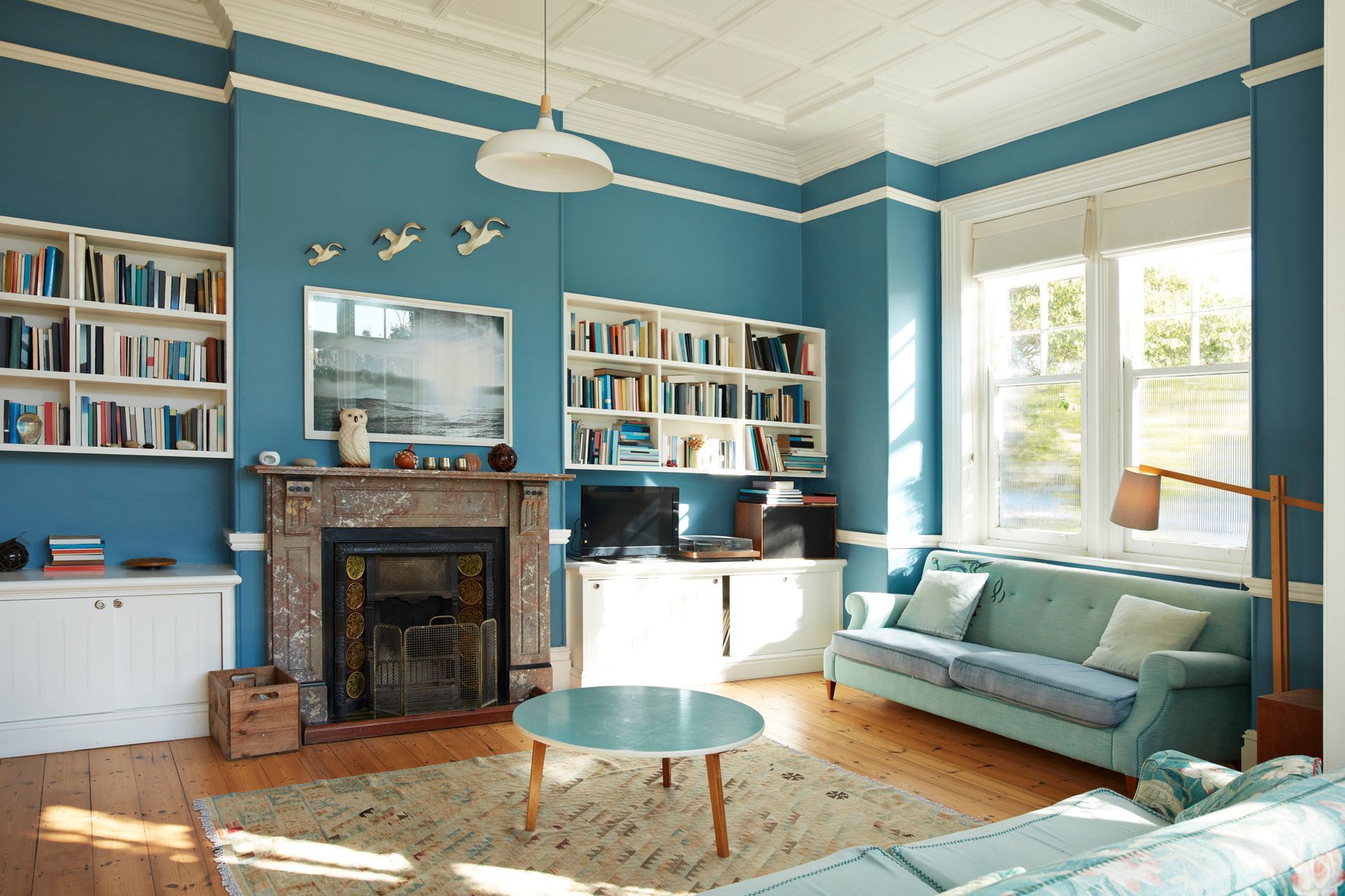 Elegant blue room with fireplace, bookshelves, and natural light.