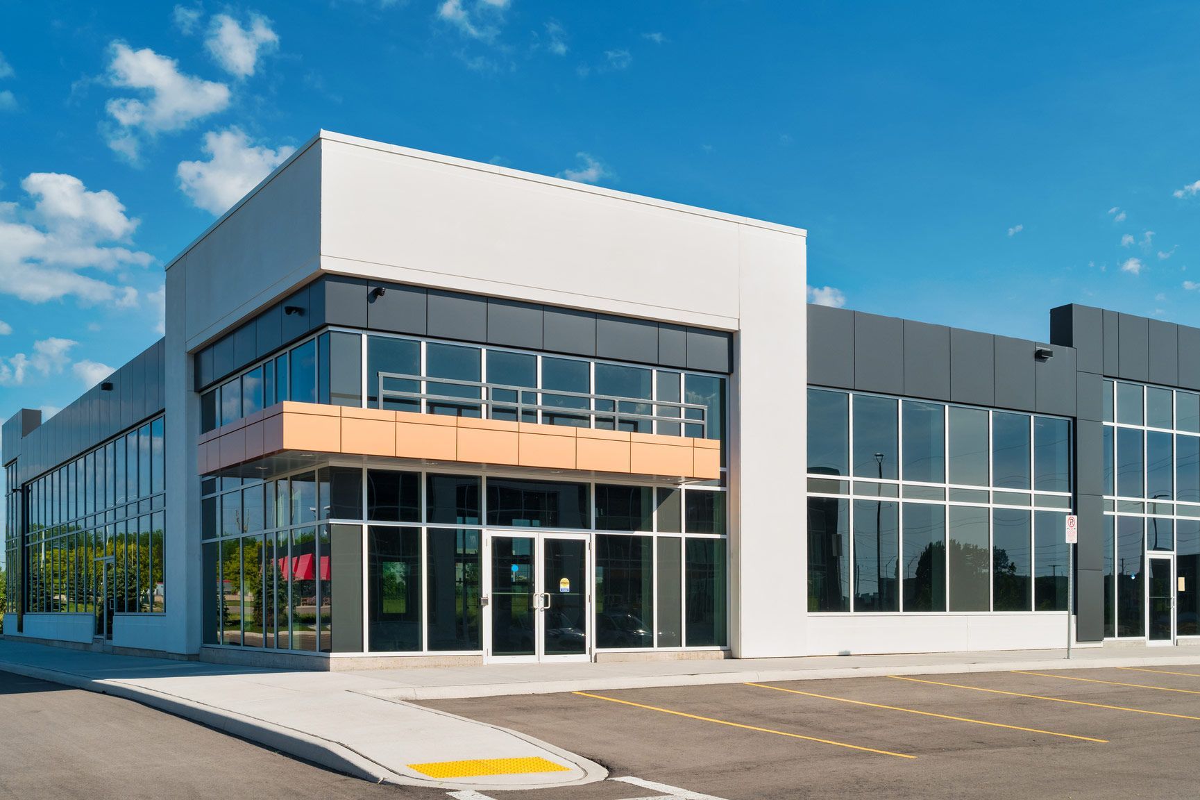 Modern commercial building with glass windows and gray and white exterior; blue sky.