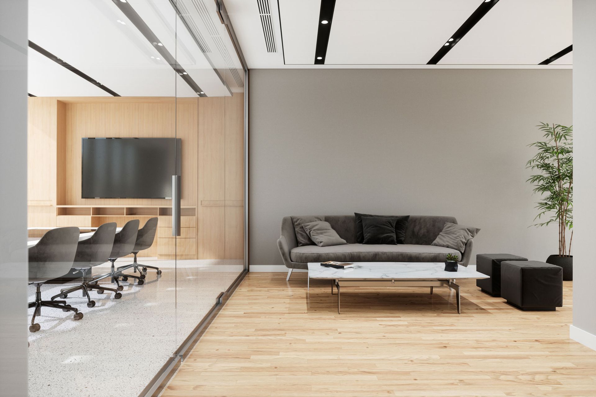Modern office lounge area with a gray sofa, coffee table, and conference room visible through glass.