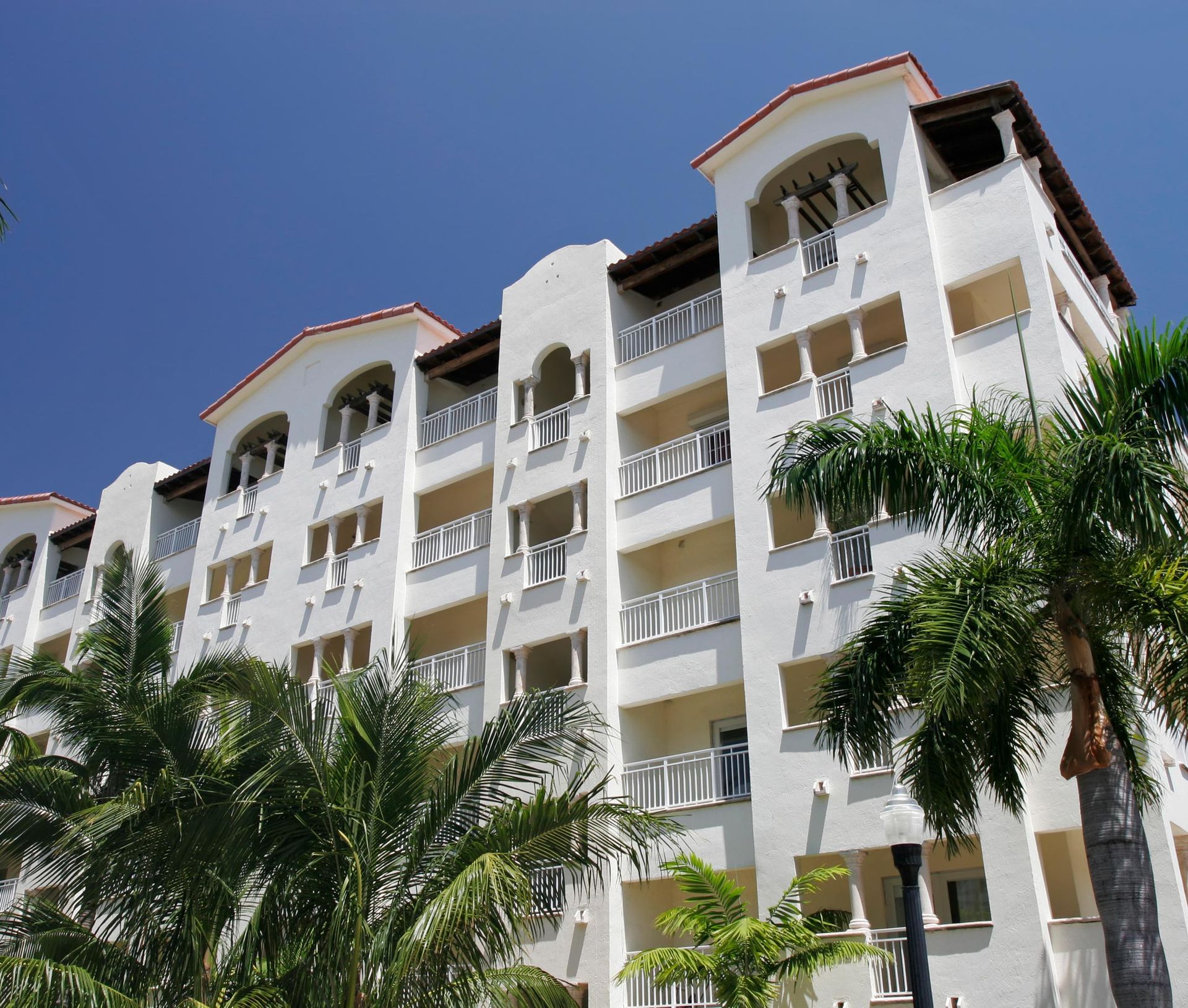 White apartment building with balconies and palm trees against a blue sky. White apartment building with balconies and palm trees against a blue sky.