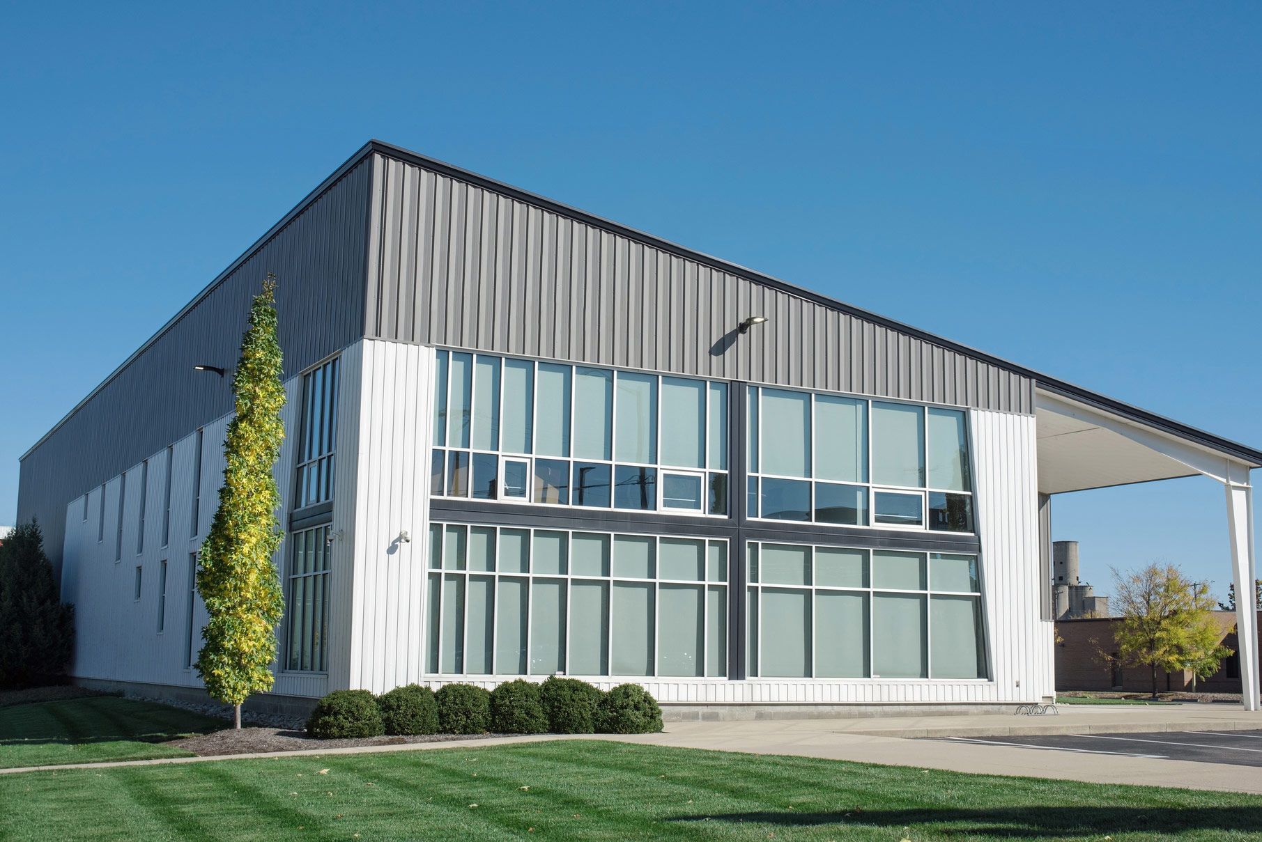 Modern building with a sloped metal roof and large windows, set on a green lawn under a blue sky.