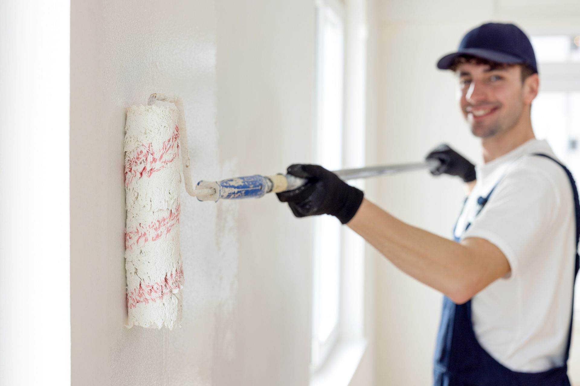 Man wearing overalls painting a bright room with a roller brush. Man wearing overalls painting a bright room with a roller brush.