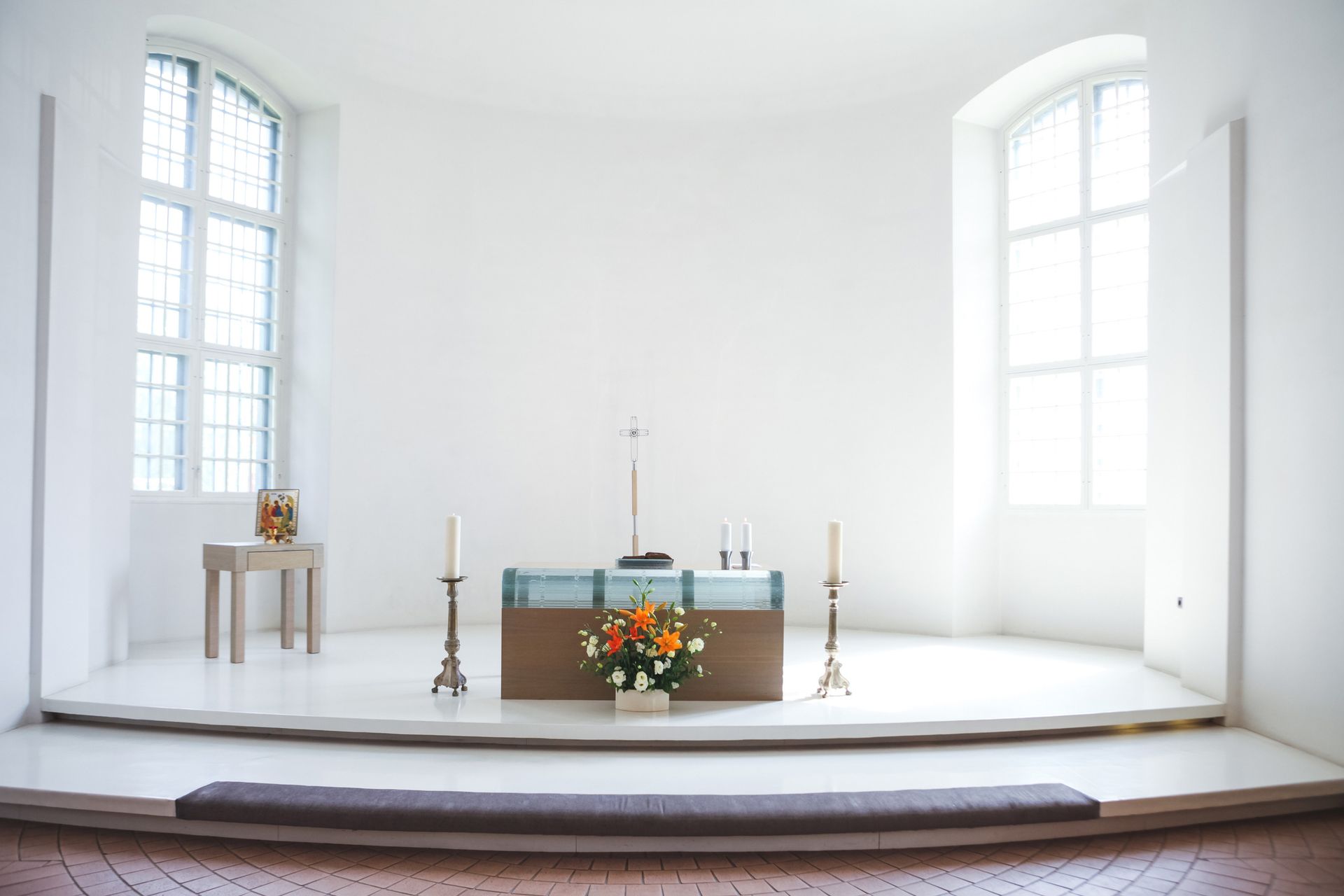 Bright, white sanctuary with an altar, two windows, flowers, and candles.