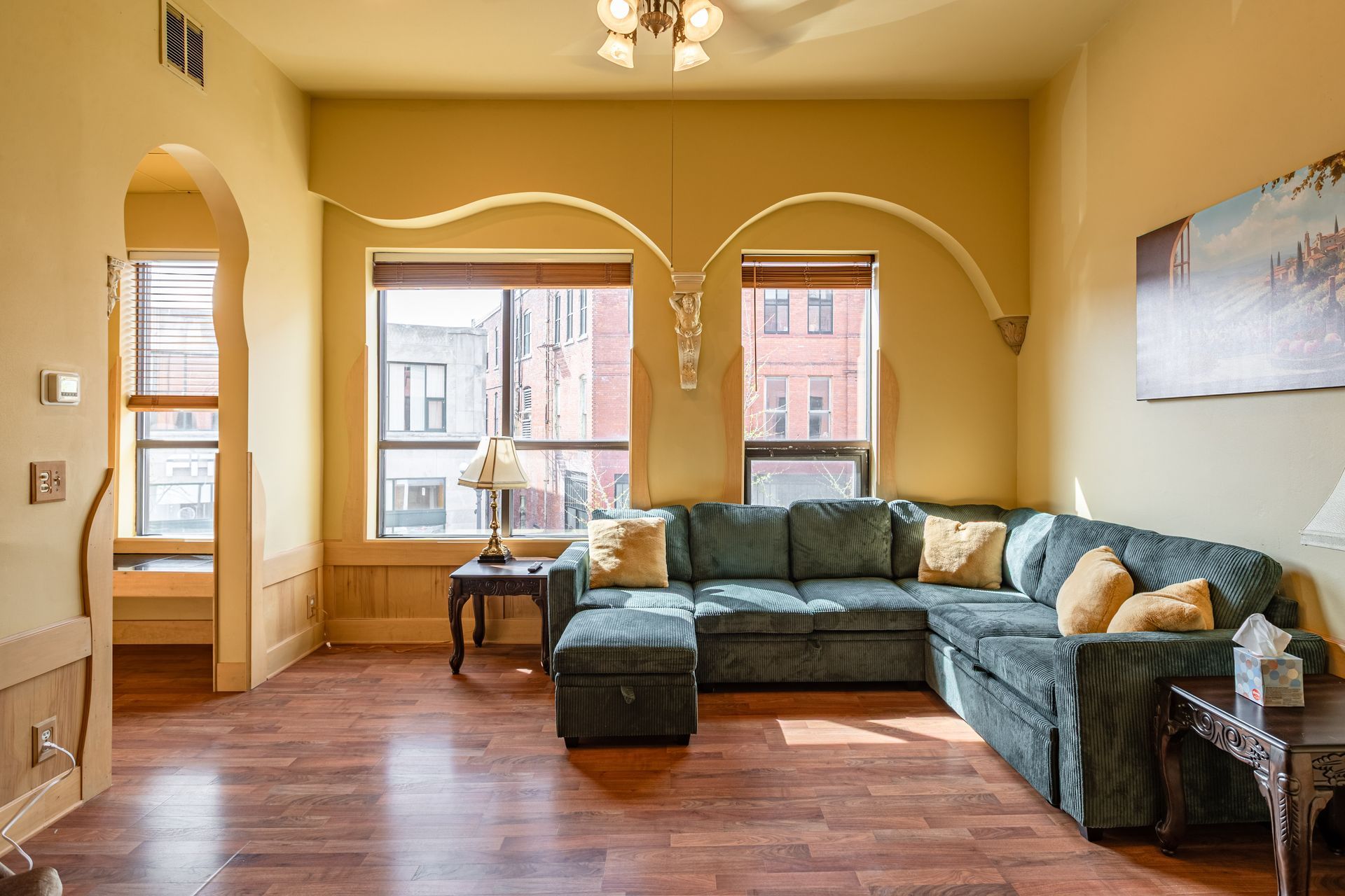 Sunlit living room with tan walls, blue sectional sofa, wood floors, and large windows