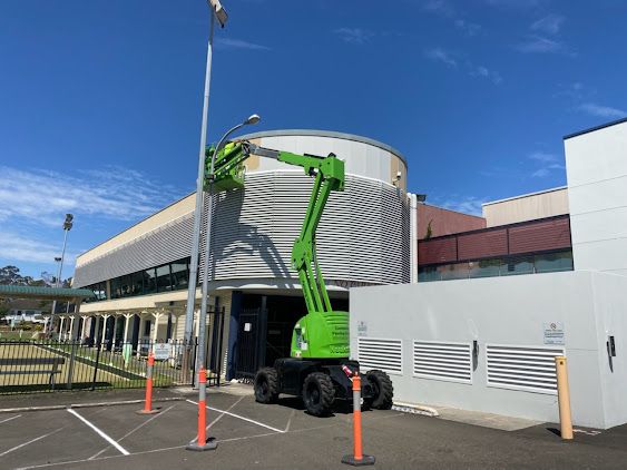 A Green Crane is Working on a Building in a Parking Lot — Commercial Painting Group in Nowra, NSW