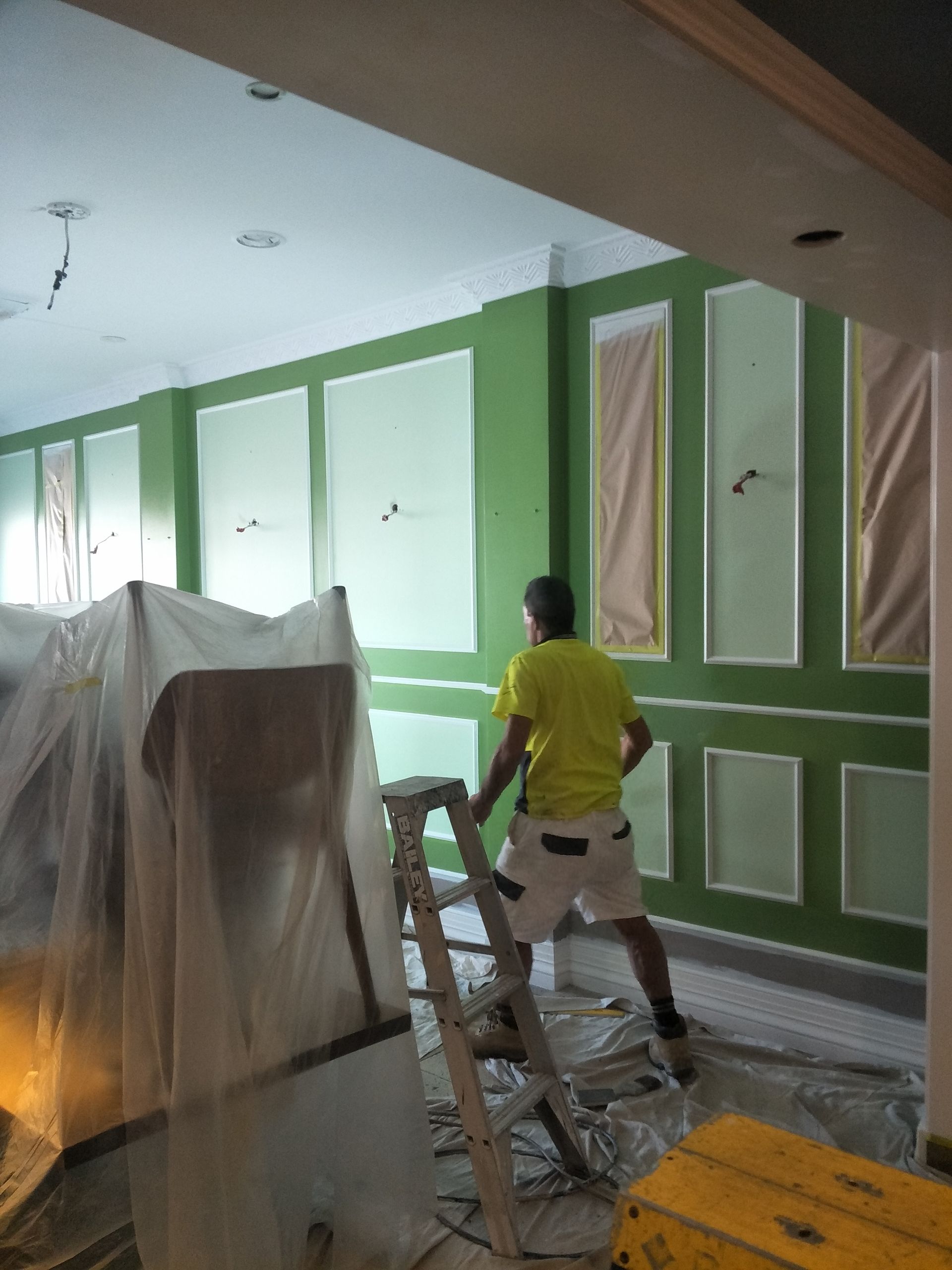 A man is walking next to a green wall— Commercial Painting Group in Goulburn, NSW
