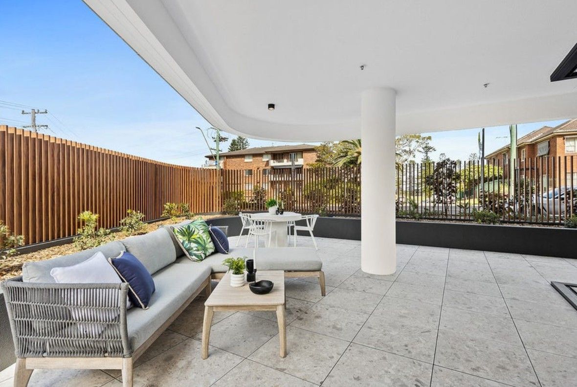 An outdoor area with a grey couch and a wooden table, and a large white pole — Commercial Painting Group in Kembla Grange, NSW
