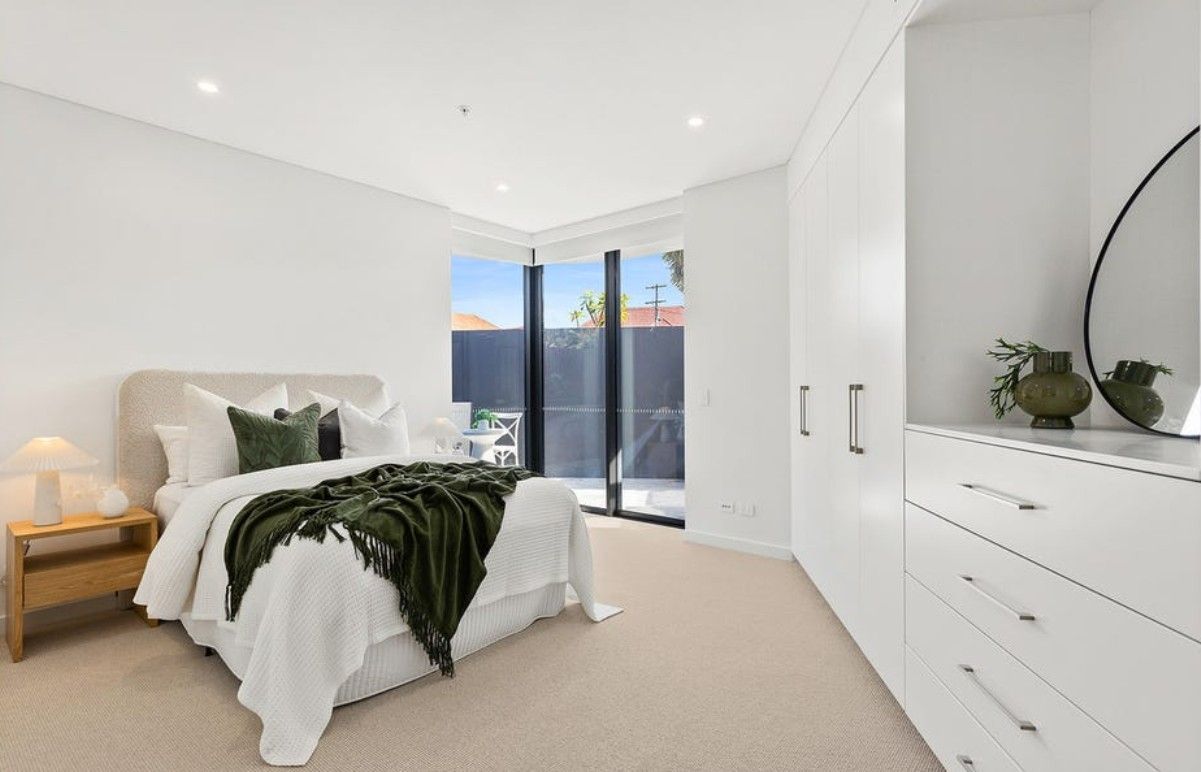A bedroom with white walls and cupboards, and a bed with a green blanket — Commercial Painting Group in Kembla Grange, NSW