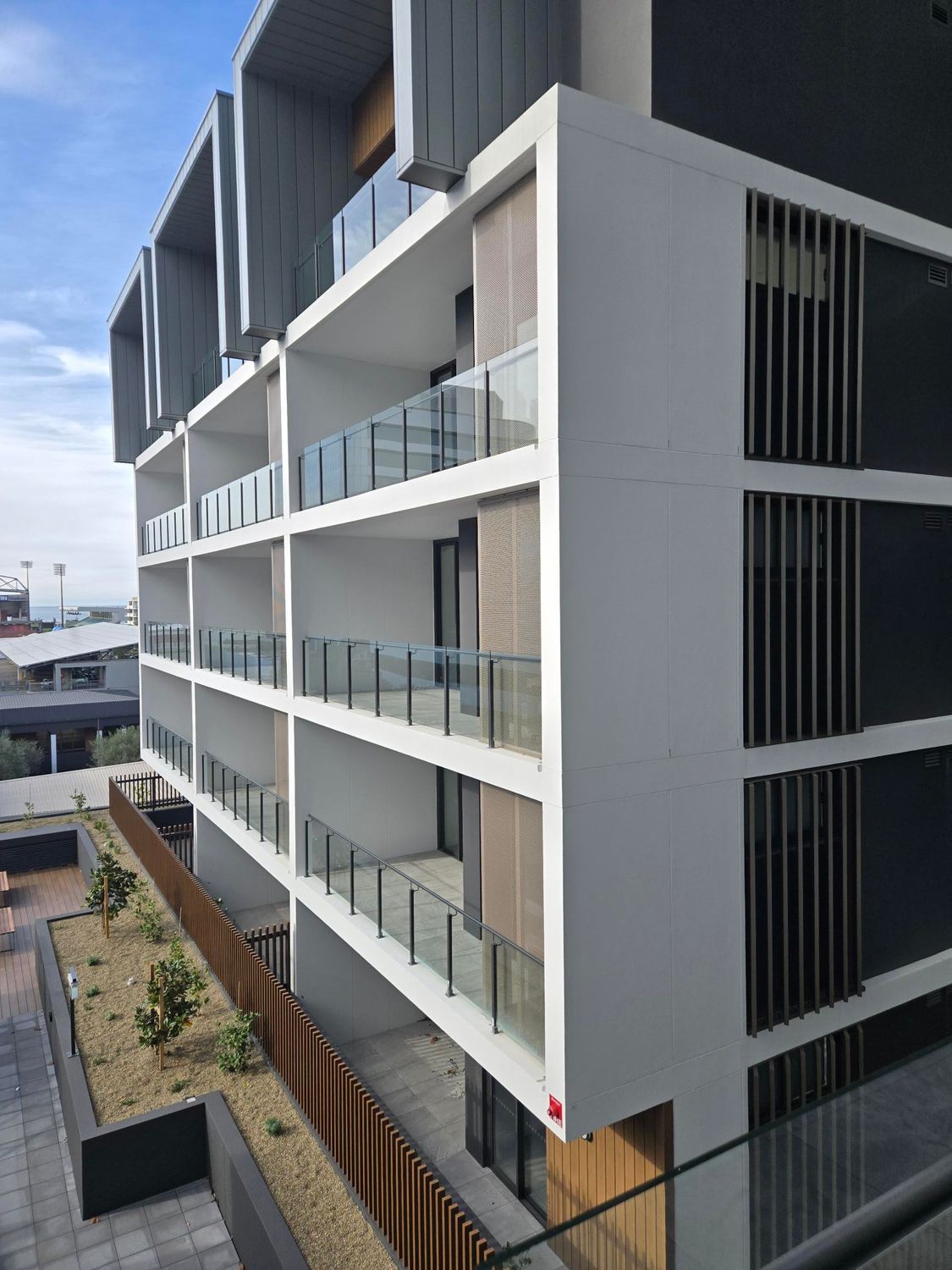 A side view of a white apartment block An outdoor area with pavers and a raised garden bed with the sun setting — Commercial Painting Group in Kembla Grange, NSW