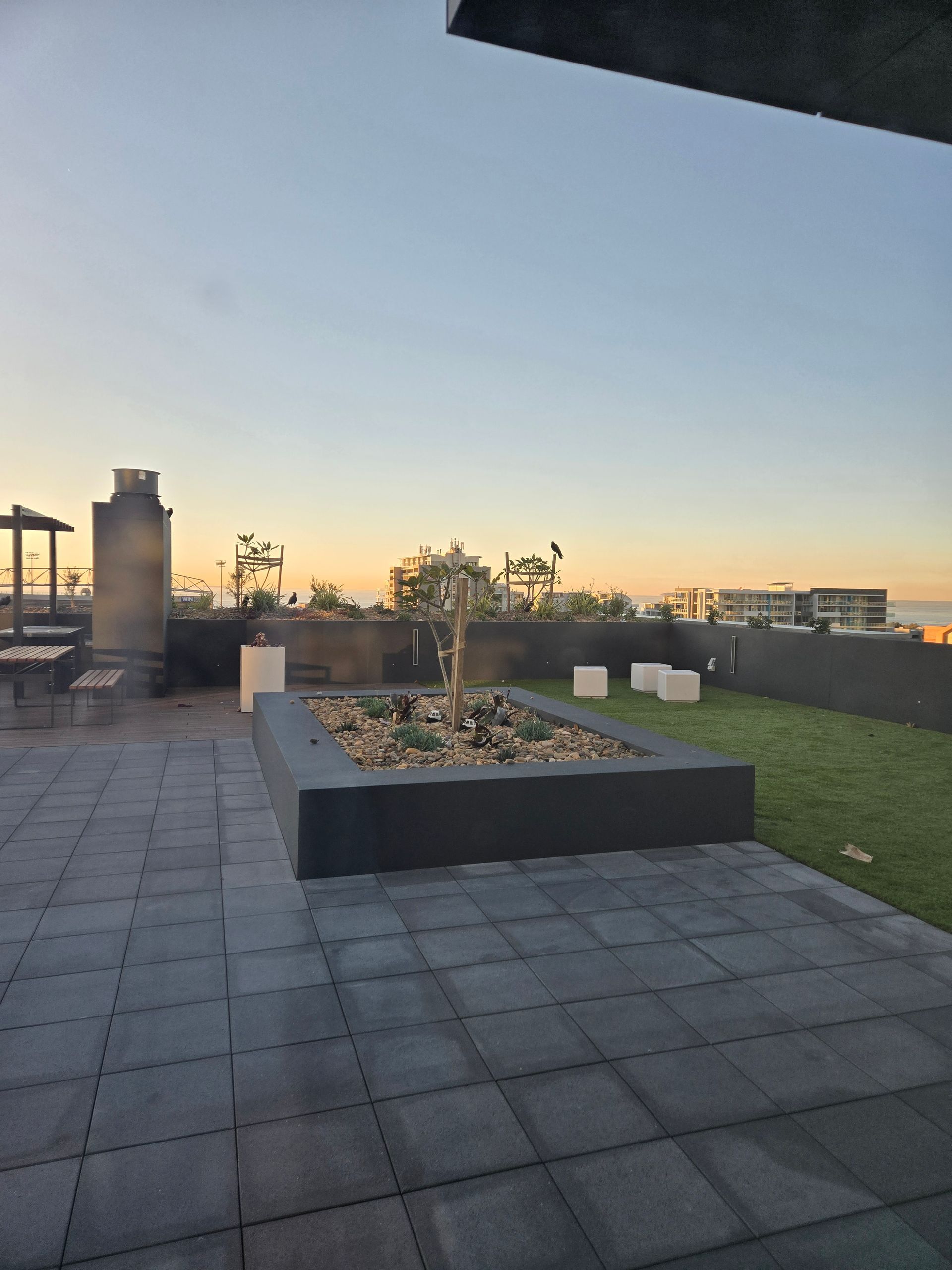 An outdoor area with pavers and a raised garden bed with the sun setting — Commercial Painting Group in Kembla Grange, NSW