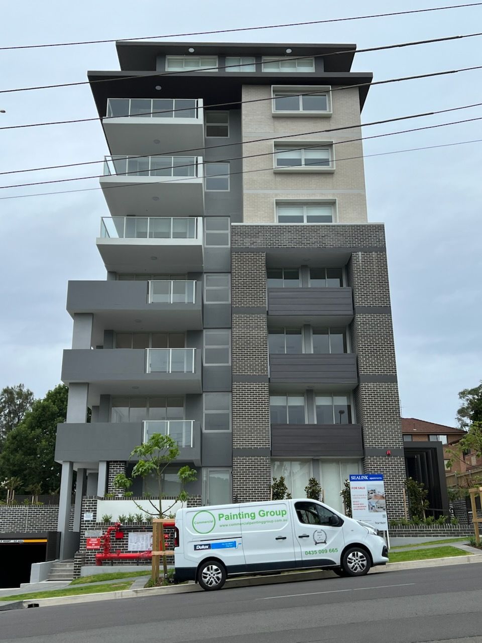 A white van is parked in front of a grey apartment block — Commercial Painting Group in Kembla Grange, NSW