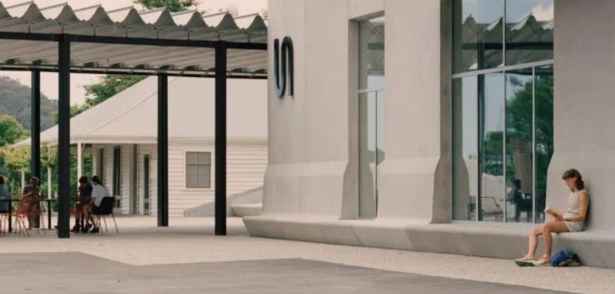 A woman is sitting on a bench in front of a building reading a book — Commercial Painting Group in Kembla Grange, NSW