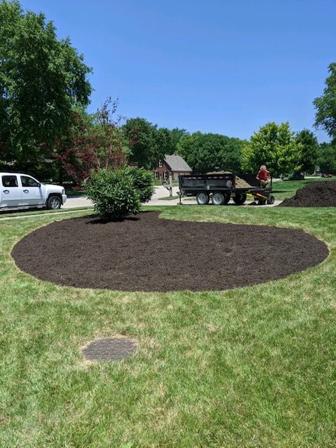 A freshly mulched landscaping bed in a yard. A truck and person are nearby.