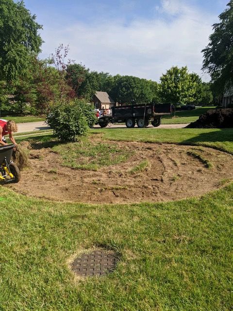 A circular garden bed being prepared for planting; a truck is parked nearby.