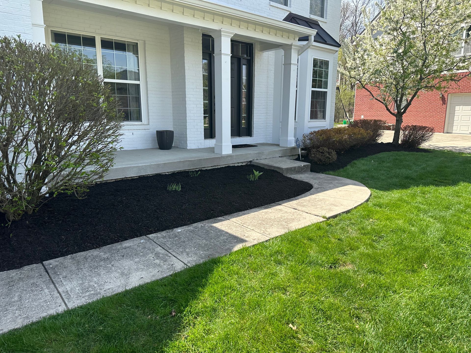 Front of a house with a black mulched flower bed, concrete walkway, and green grass.