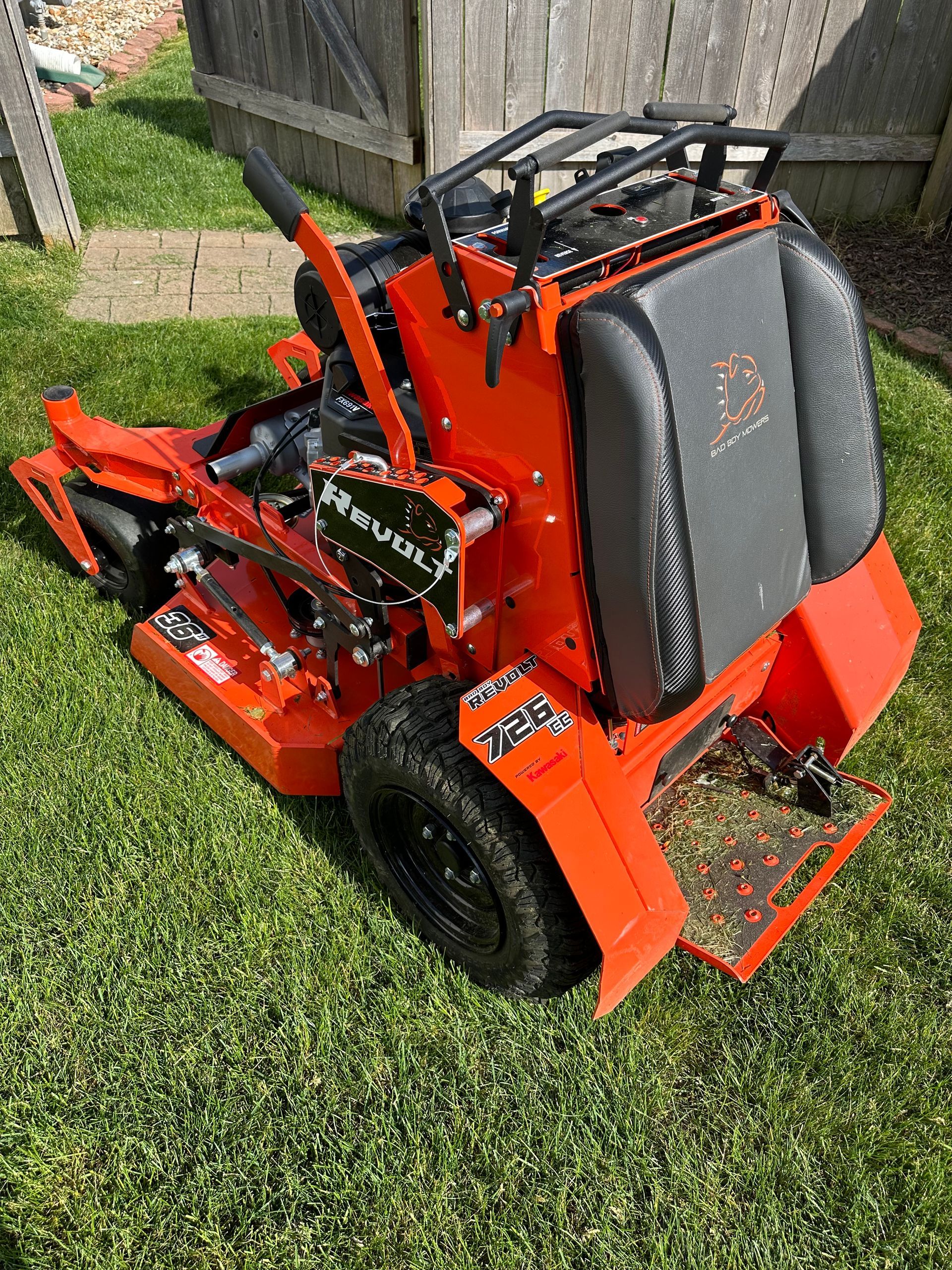 Orange and black stand-on zero-turn lawnmower on green grass.