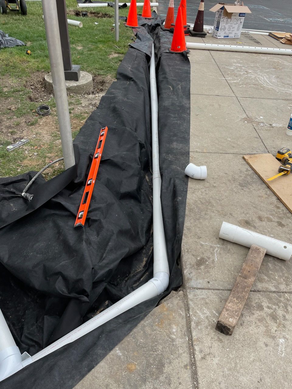 Construction site with white PVC pipes and level on black fabric next to a sidewalk.