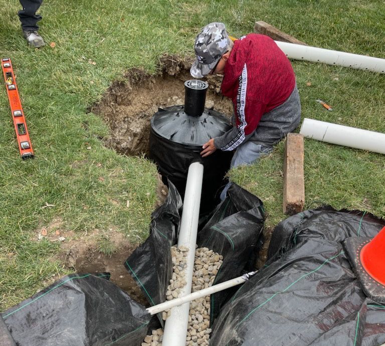 A person in a red shirt installing a drainage system in a yard.