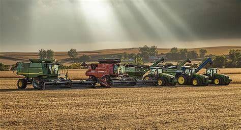 Four farm combines lined up in a golden field under a cloudy sky