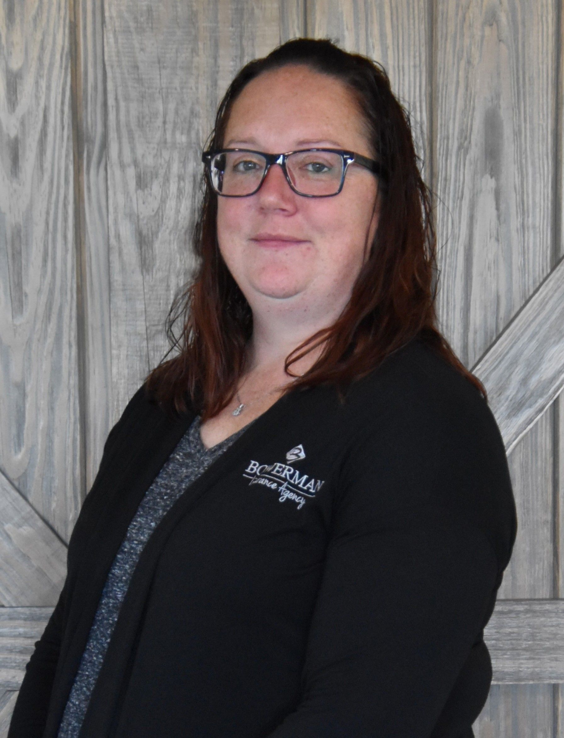 Woman wearing glasses and black sweater smiles in front of a wood-paneled wall.