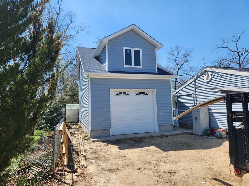 A small blue garage with a white garage door is being built next to a house.