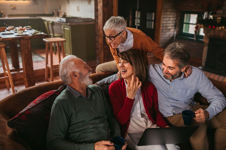 Four people smiling and chatting on a couch in a cozy living room with warm lighting
