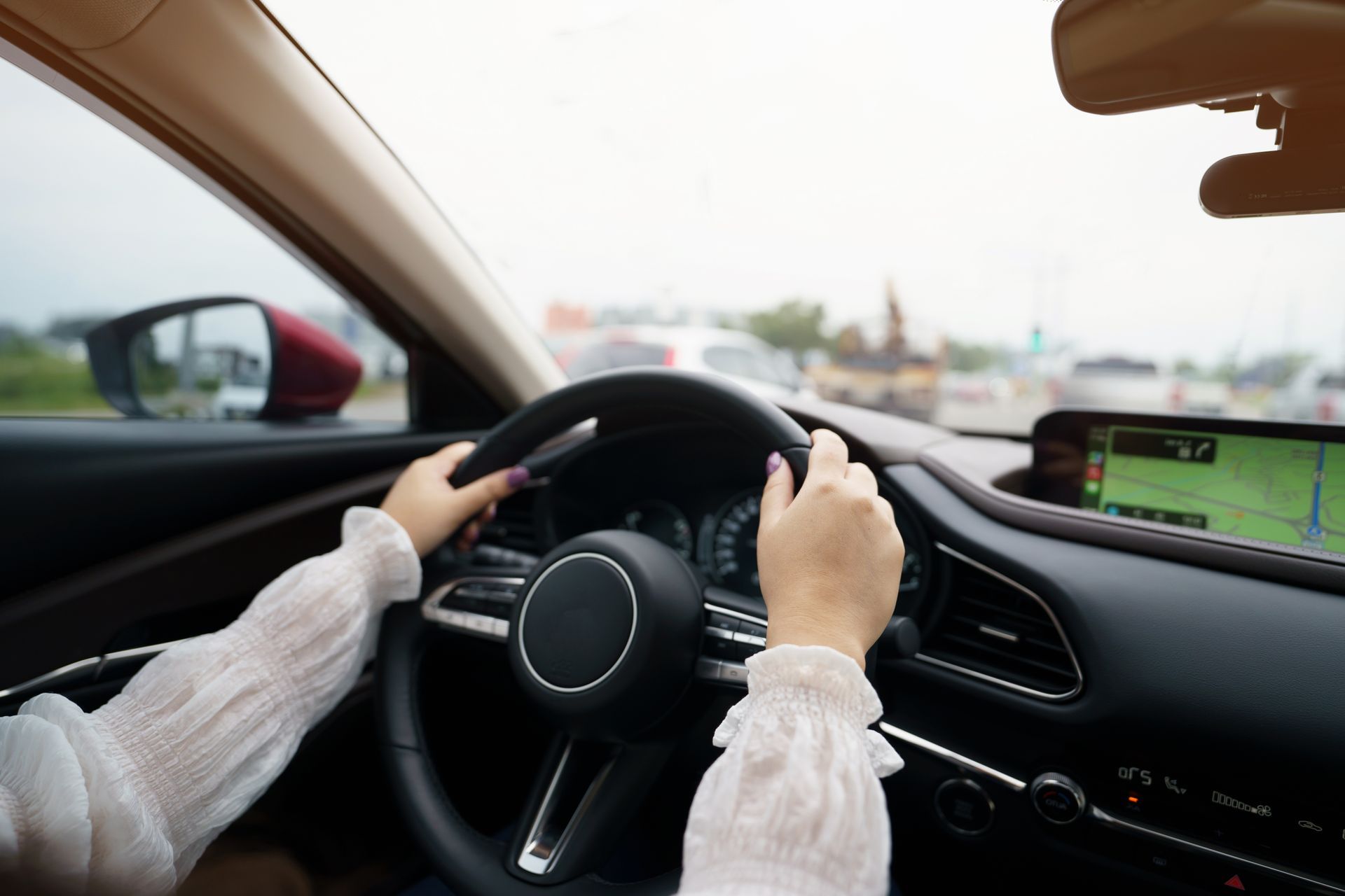 Driver holding steering wheel inside a car, with dashboard and road visible ahead.