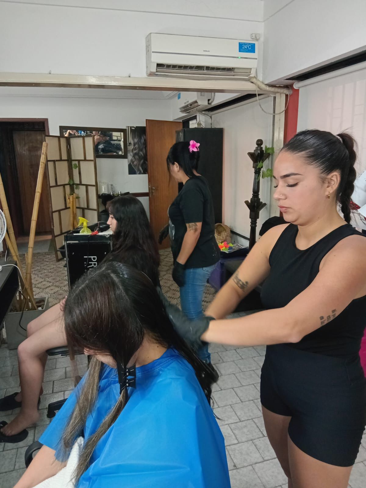 Una estilista seca con secador el largo cabello castaño de una clienta en un salón moderno.