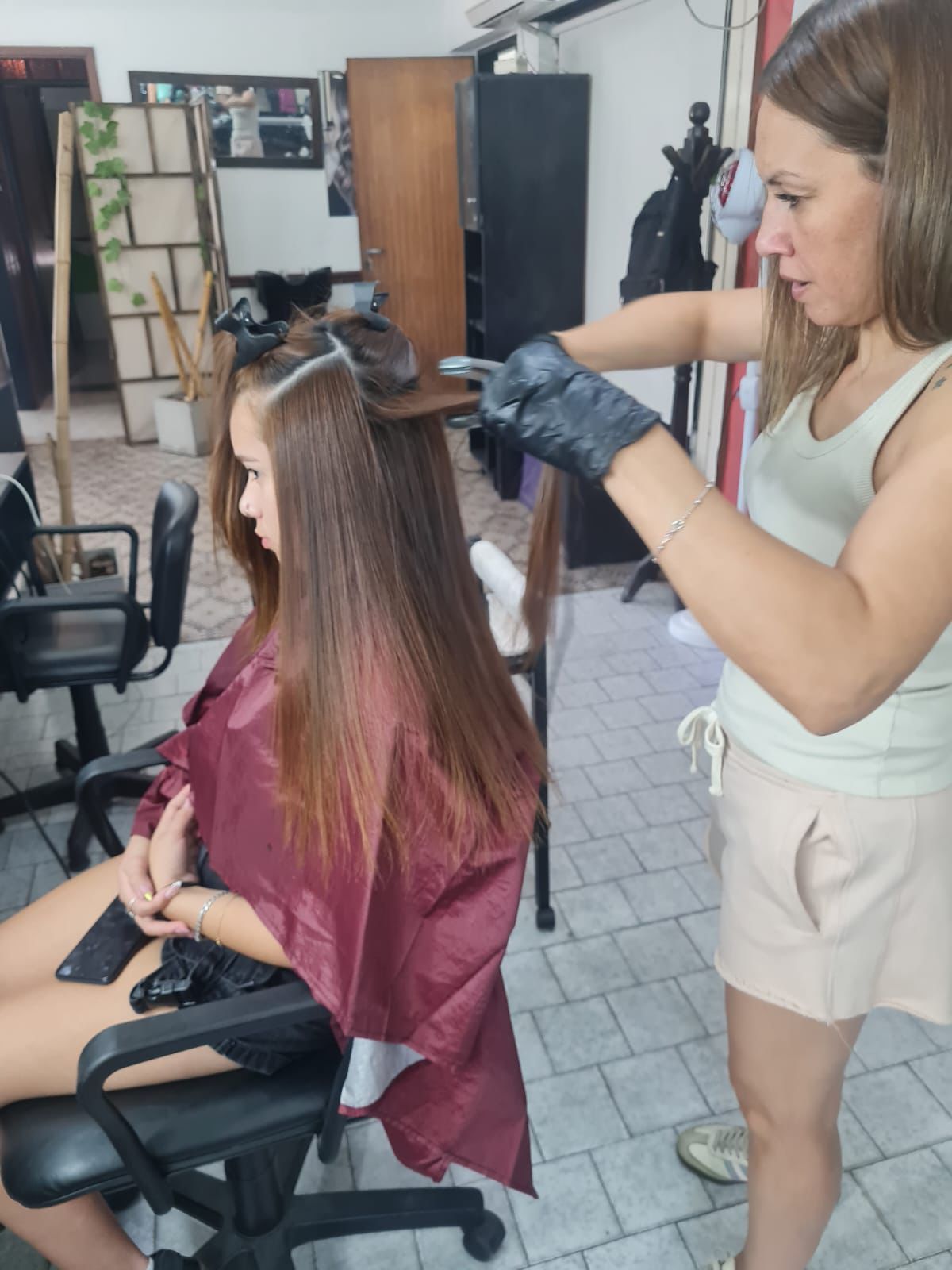 Peluquera aplicando un tratamiento a una clienta sentada en un salón luminoso.