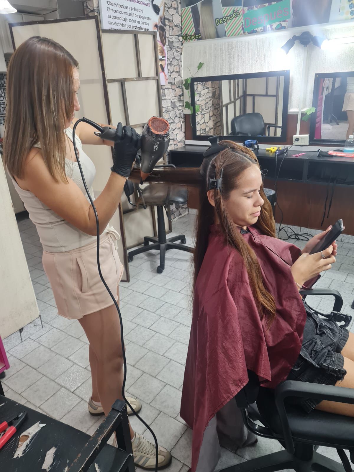 Una peluquera corta el pelo a una clienta en un salón luminoso y moderno con espejos y sillas de color beige.