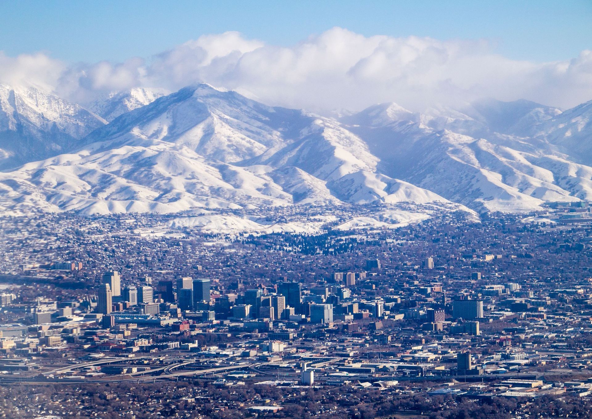 Snow-covered mountains behind a dense city skyline under a hazy blue sky