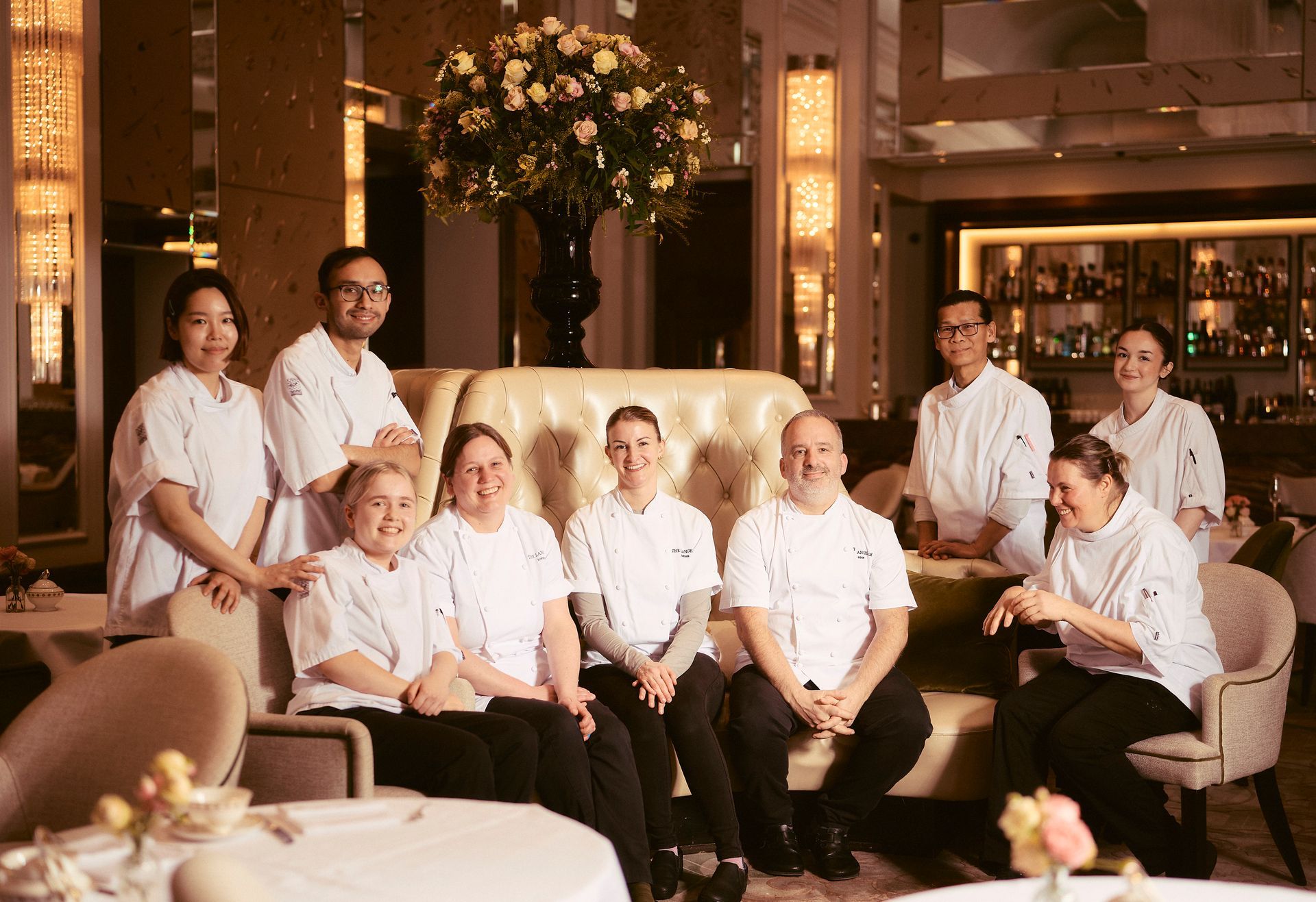 Group of hospitality staff posing in a warmly lit hotel lounge with a large sofa and floral arrangement.