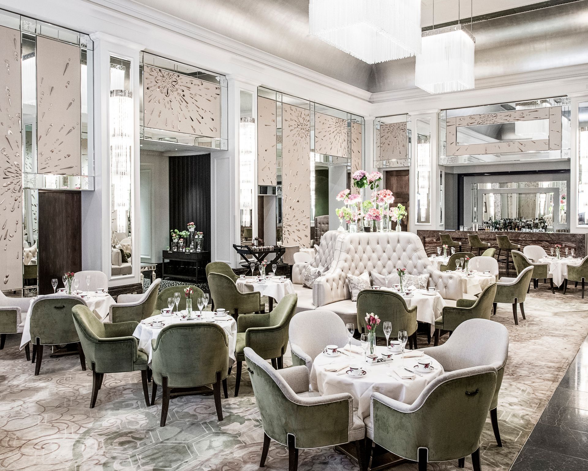 Elegant restaurant dining room with plush green chairs, white tablecloths, mirrored walls, and chandeliers
