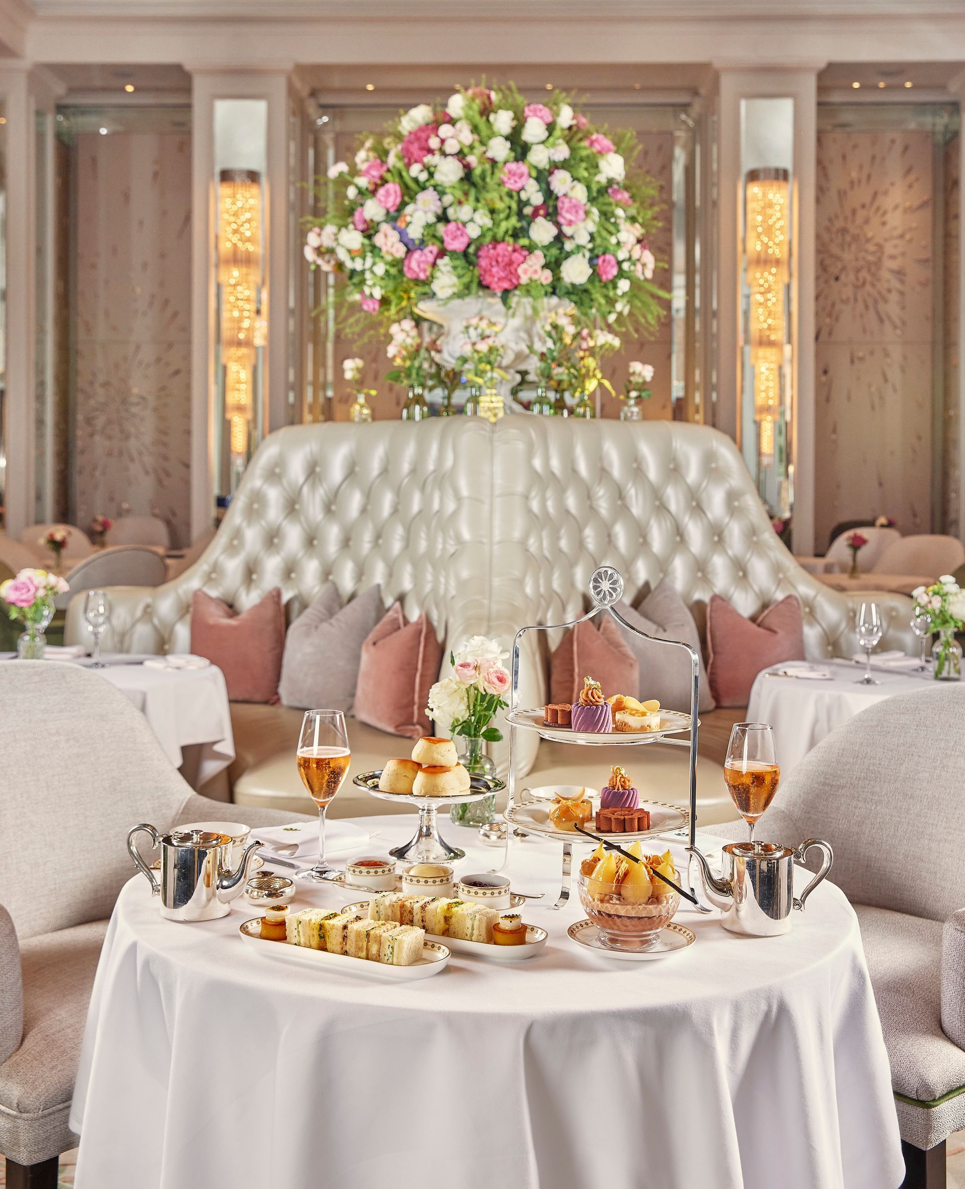 Elegant tea table in a luxurious pink-and-cream lounge with flowers and desserts on tiered stands