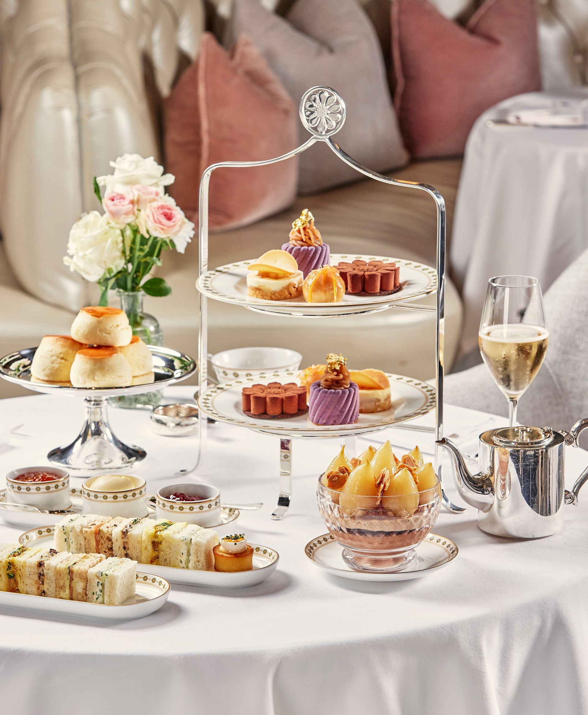 Elegant tea party table with tiered pastries, fruit tarts, glasses, and white floral decor