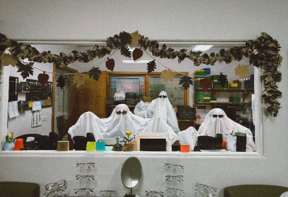 Window display with four ghosts wearing sunglasses, fall garland, various objects.