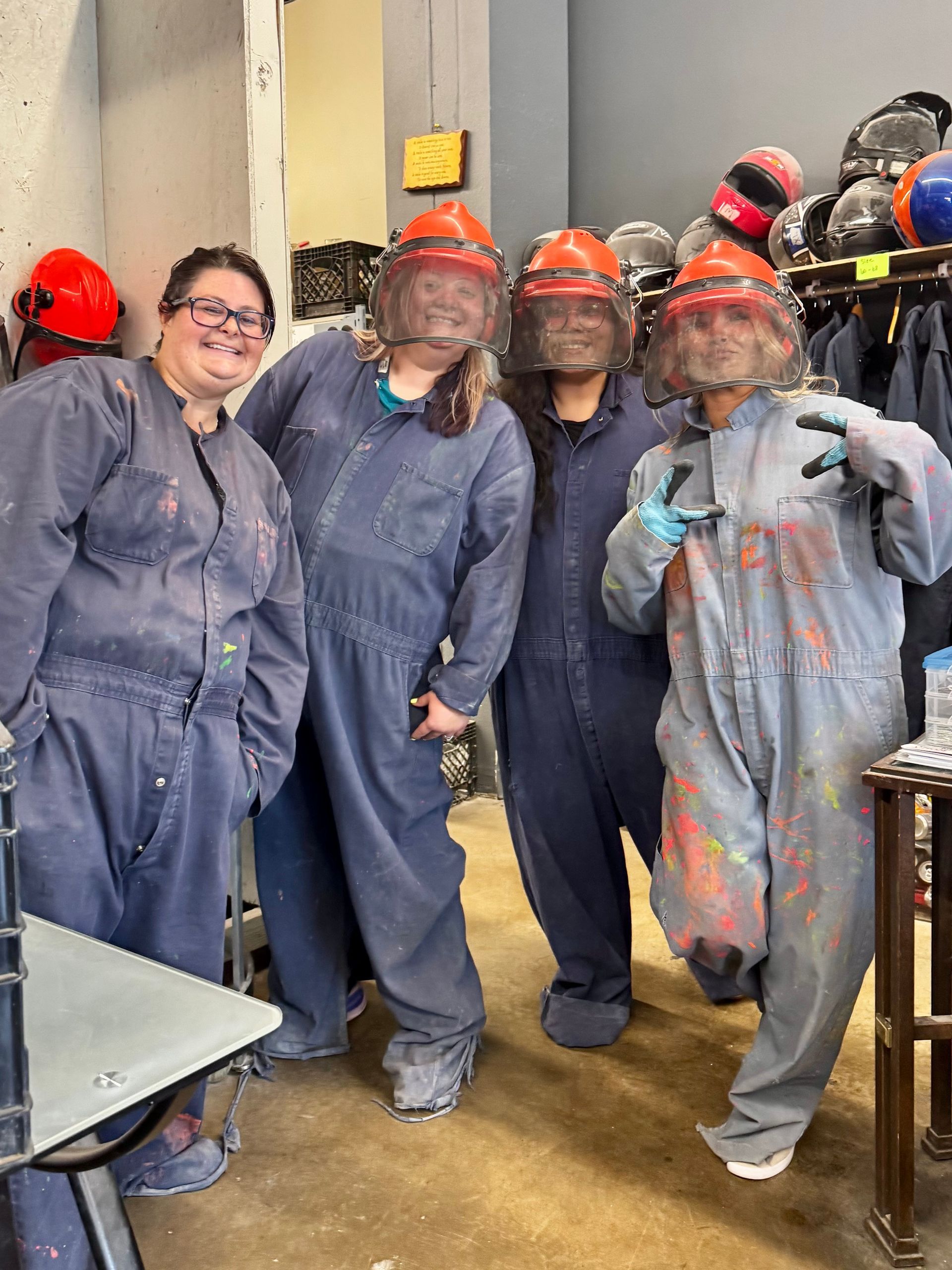 Five people in safety gear and blue coveralls pose indoors, wearing hard hats and face shields.