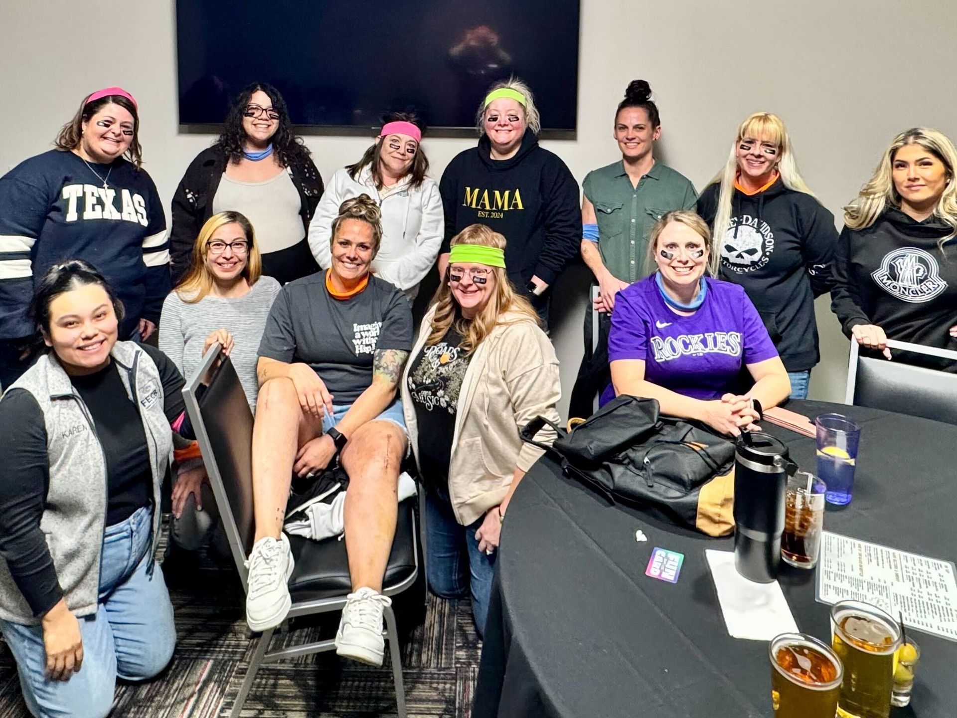 Group of women pose indoors, many wearing bandanas, some with face paint.