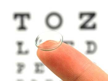 Contact lens on a finger, with a blurred eye chart in the background.