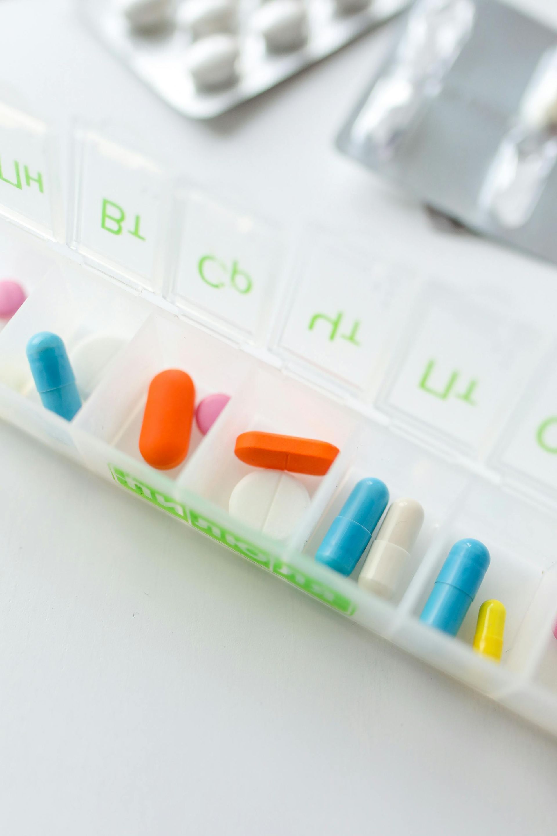 Pill organizer with various colored pills and medication blister packs in the background.