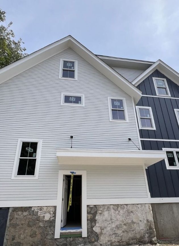 A house exterior under construction with horizontal light grey wavy siding and vertical dark blue board-and-batten siding.